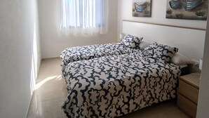 Een slaapkamer met een bed, een raam met dunne gordijnen, een wandlamp en twee schilderijen van boten.