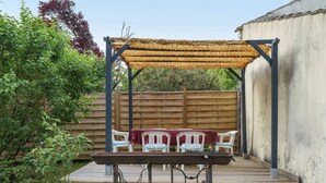 A wooden deck with a table and chairs, a pergola with a woven roof, and a wooden fence in the background.