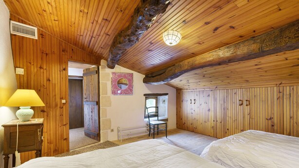 A wooden-paneled room with two beds, a chair, a lamp, and a mirror on the wall.
