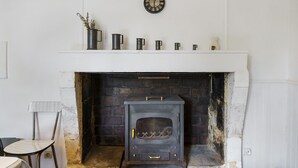 A fireplace with a clock above it, a chair to the left, and a shelf with items.
