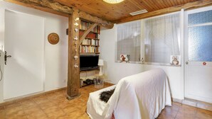 A cozy room with a wooden ceiling, a bookshelf, a television, a bed with a white cover, and a window with blinds.