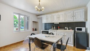 A kitchen with white cabinets, a dining table with chairs, a chandelier, and a window with a view of greenery.