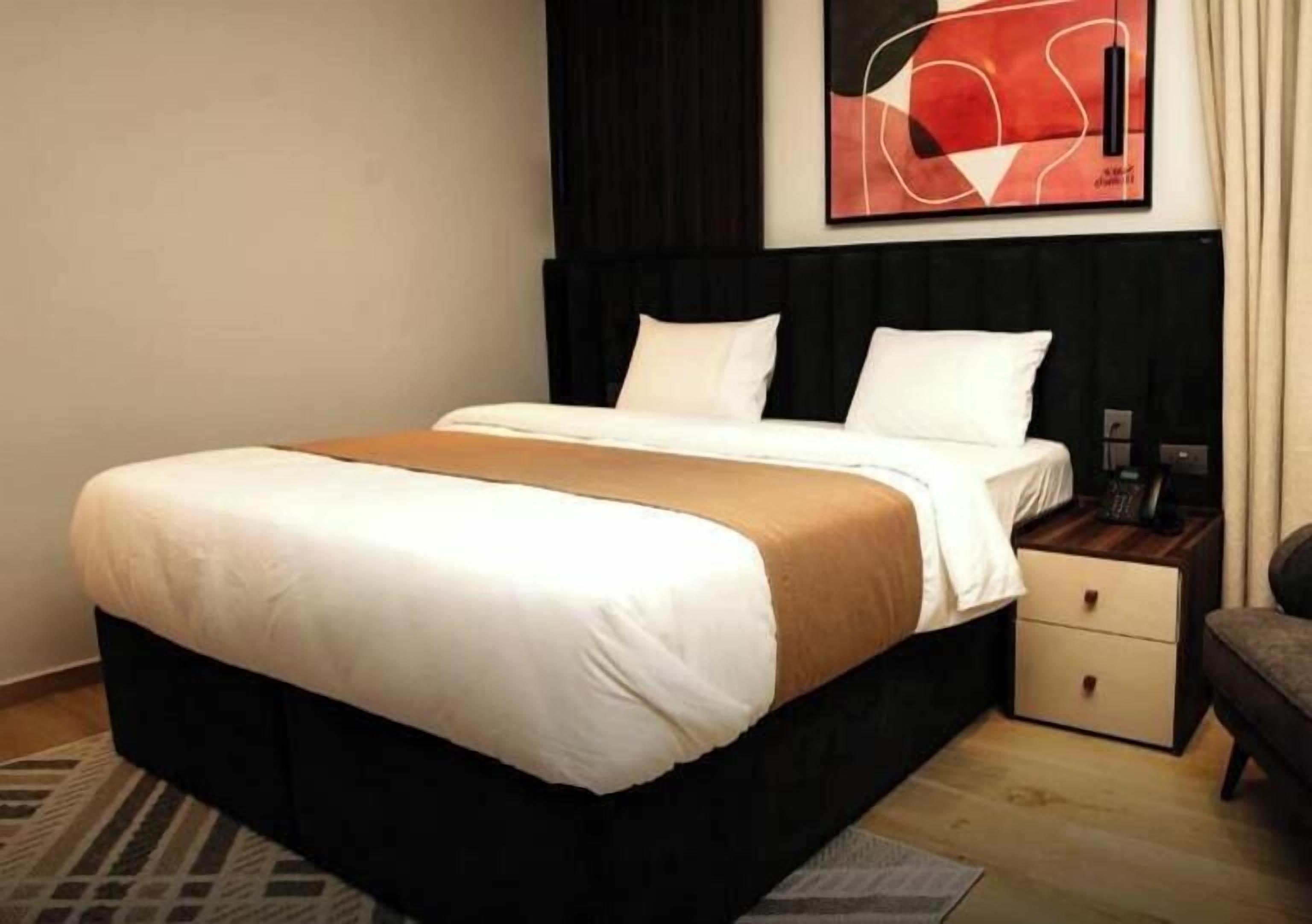 A hotel room with a bed, a nightstand, a chair, and a painting on the wall.