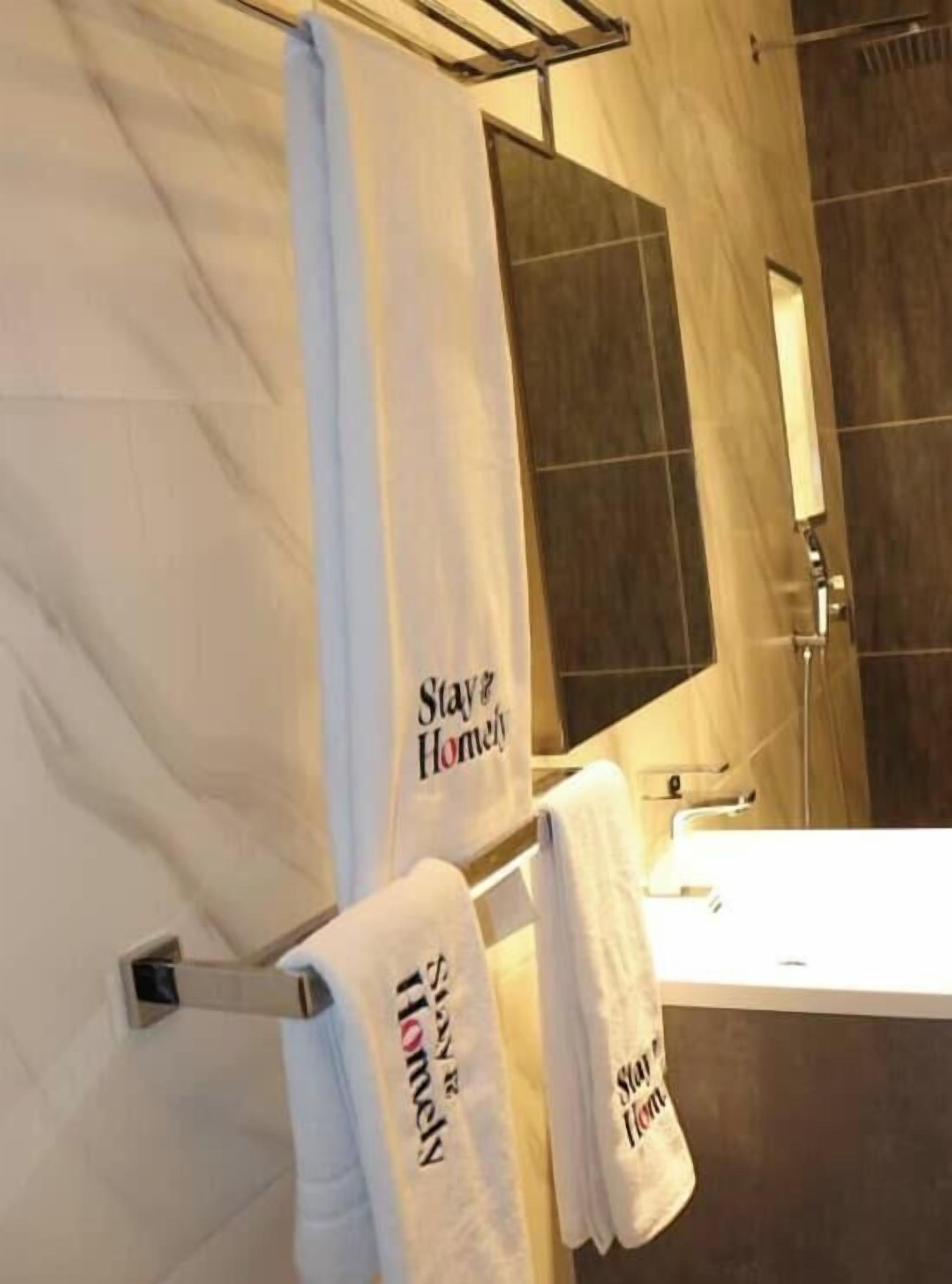 Un baño con lavamanos blanco, un espejo y toallas colgadas en un perchero.