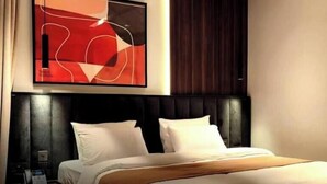 Una habitación de hotel con una cama, cabecera, una obra de arte colgada en la pared y una mesita de noche.