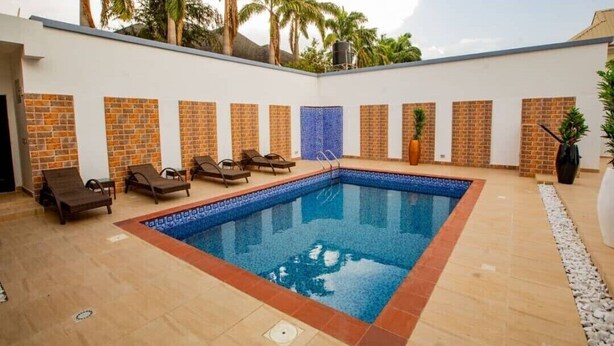 Una piscina rectangular con borde de azulejos, rodeada de sillas de descanso y un muro de ladrillo.