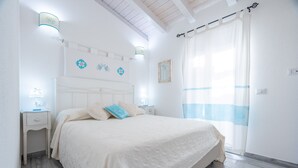Ein Schlafzimmer mit einem Bett, Nachttischen, Wandleuchten, einem Fenster mit Vorhängen und einer Decke mit sichtbaren Balken.