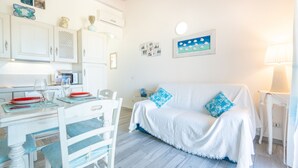 Ein Zimmer mit Esstisch, weißen Möbeln, einem weißen Sofa mit blauen Kissen und einer Wand mit gerahmten Bildern.