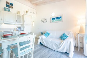 Ein Zimmer mit Esstisch, weißen Möbeln, einem weißen Sofa mit blauen Kissen und einer Wand mit gerahmten Bildern.