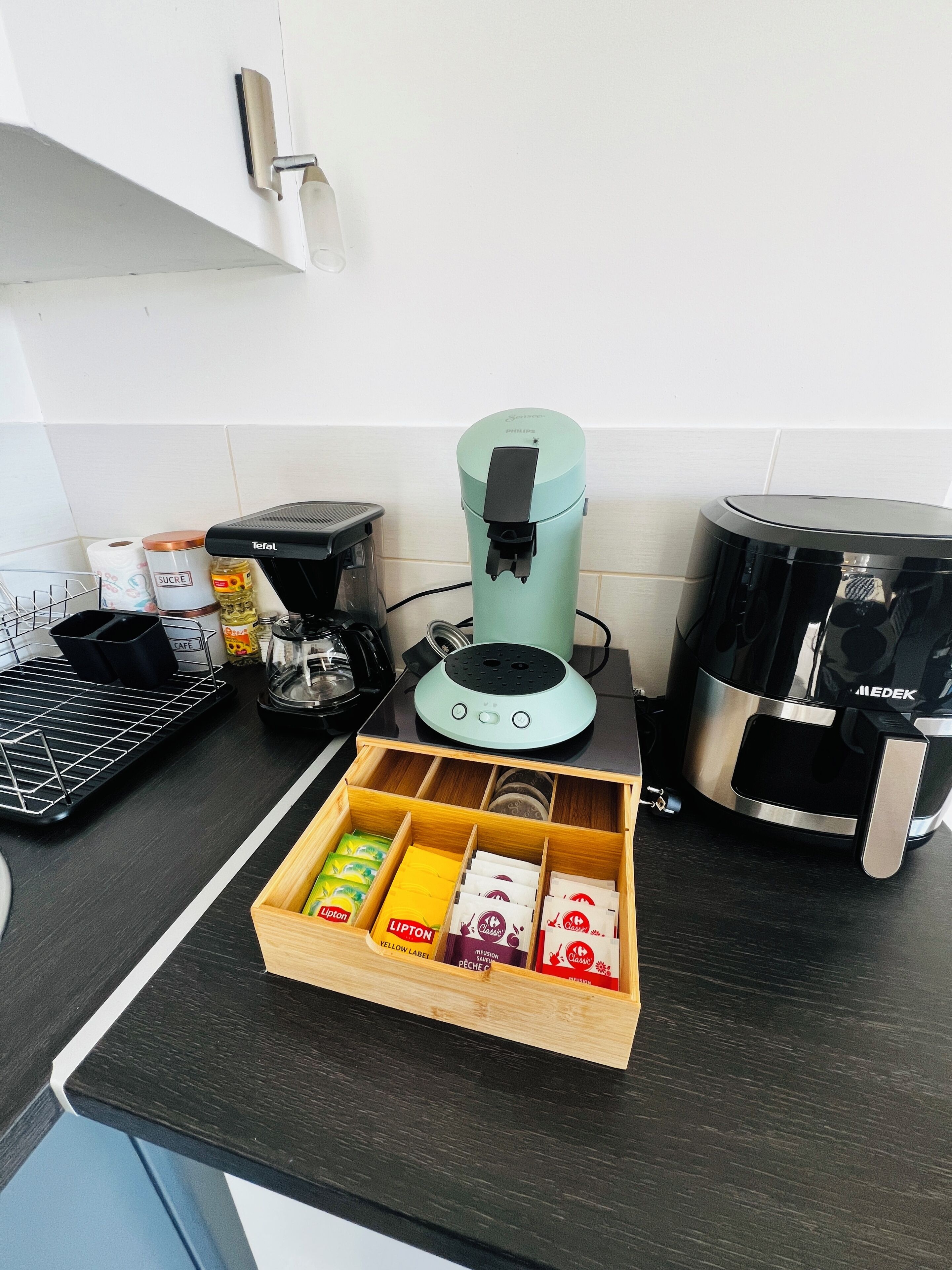 A kitchen with a coffee maker, a toaster, a kettle, and a drawer with coffee pods.