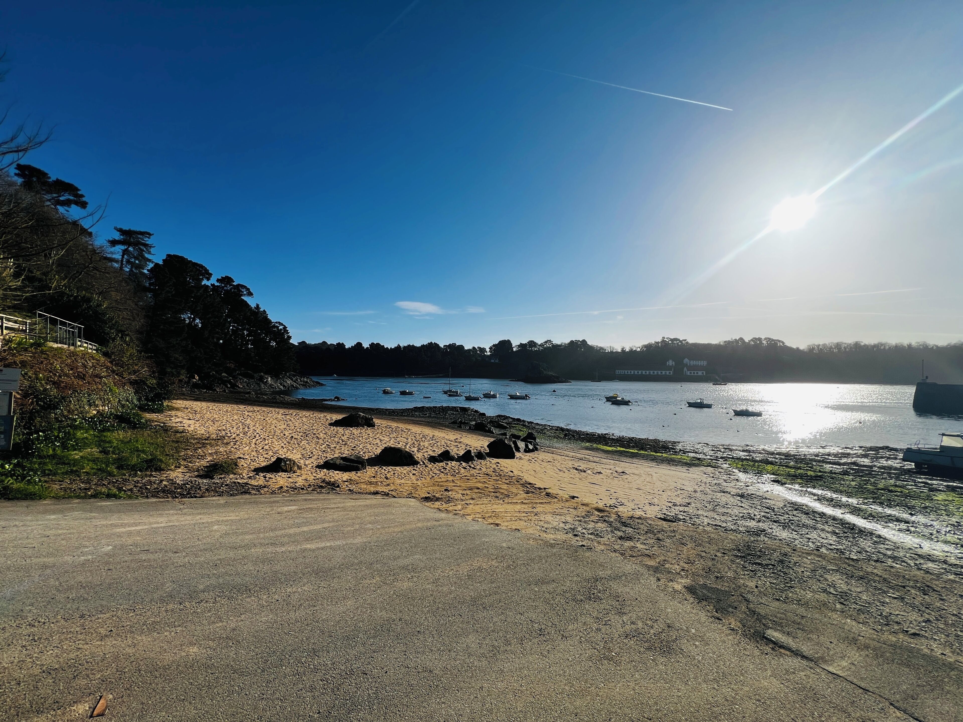 A beach with boats, a clear sky, and a sunlit path.