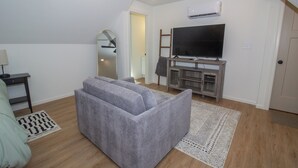 Una sala de estar con un sofá gris, un televisor de pantalla plana, un mueble de entretenimiento de madera y una alfombra estampada.