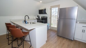 Una cocina con una isla central, taburetes de bar, microondas, estufa y refrigerador.