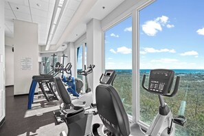 Ein Fitnessraum mit Cardiogeräten und einem großen Fenster mit Blick auf einen Strand.
