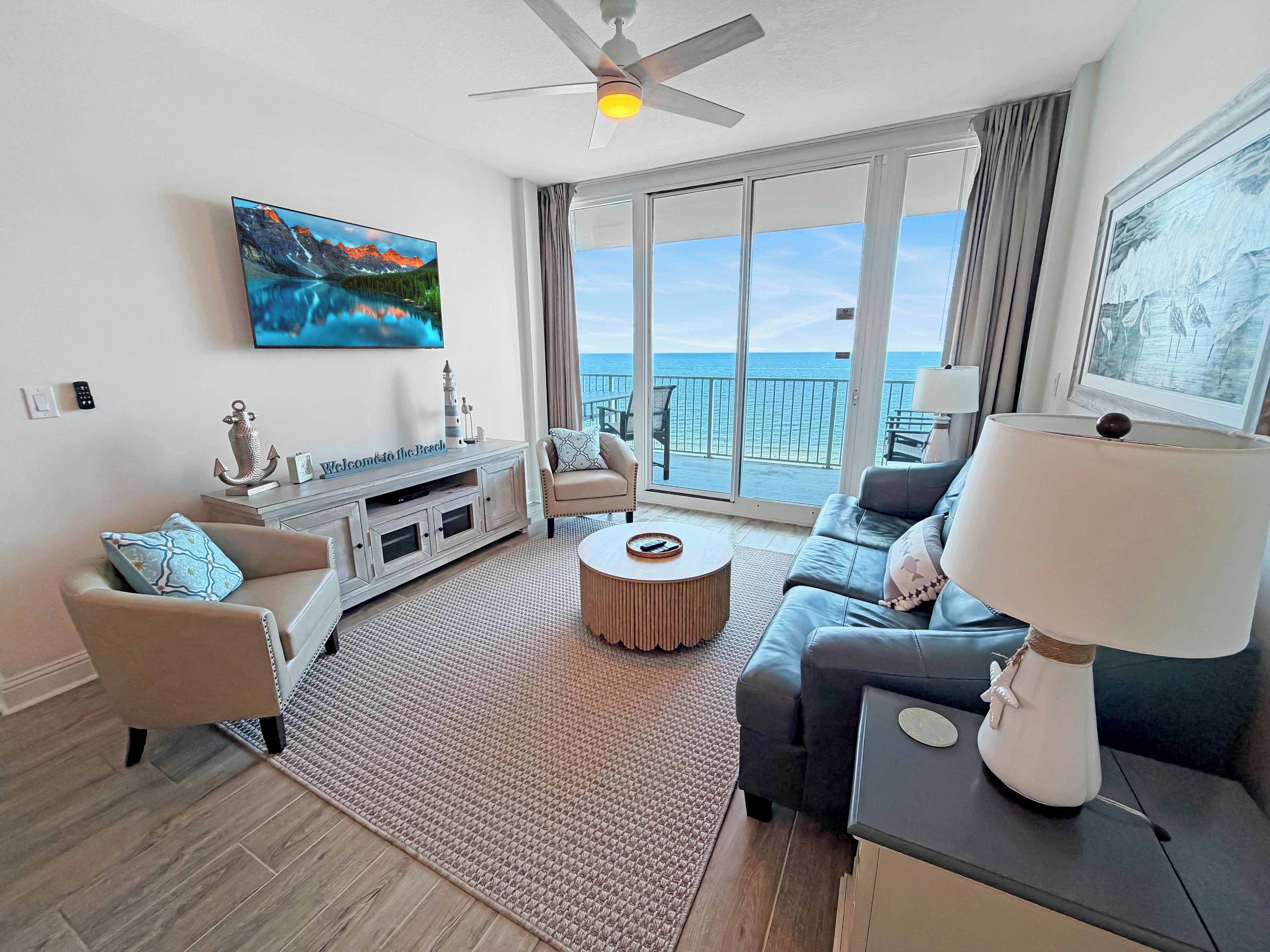 A modern living room with a large window, a ceiling fan, and a flat-screen TV.