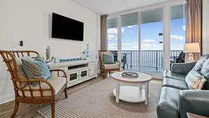Ein Wohnzimmer mit Fernseher, Korbsesseln, einem runden Couchtisch und einem Balkon mit Blick.