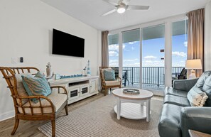 A living room with a TV, wicker chairs, a round coffee table, and a balcony with a view. - New owner, newly renovated - Beachfront condo - 2br + Bnkrm 8th floor great view (Gulf Shores)