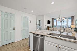 A modern kitchen with a built-in dishwasher, a dining area with a chandelier, and a view of the ocean. - New owner, newly renovated - Beachfront condo - 2br + Bnkrm 8th floor great view (Gulf Shores)