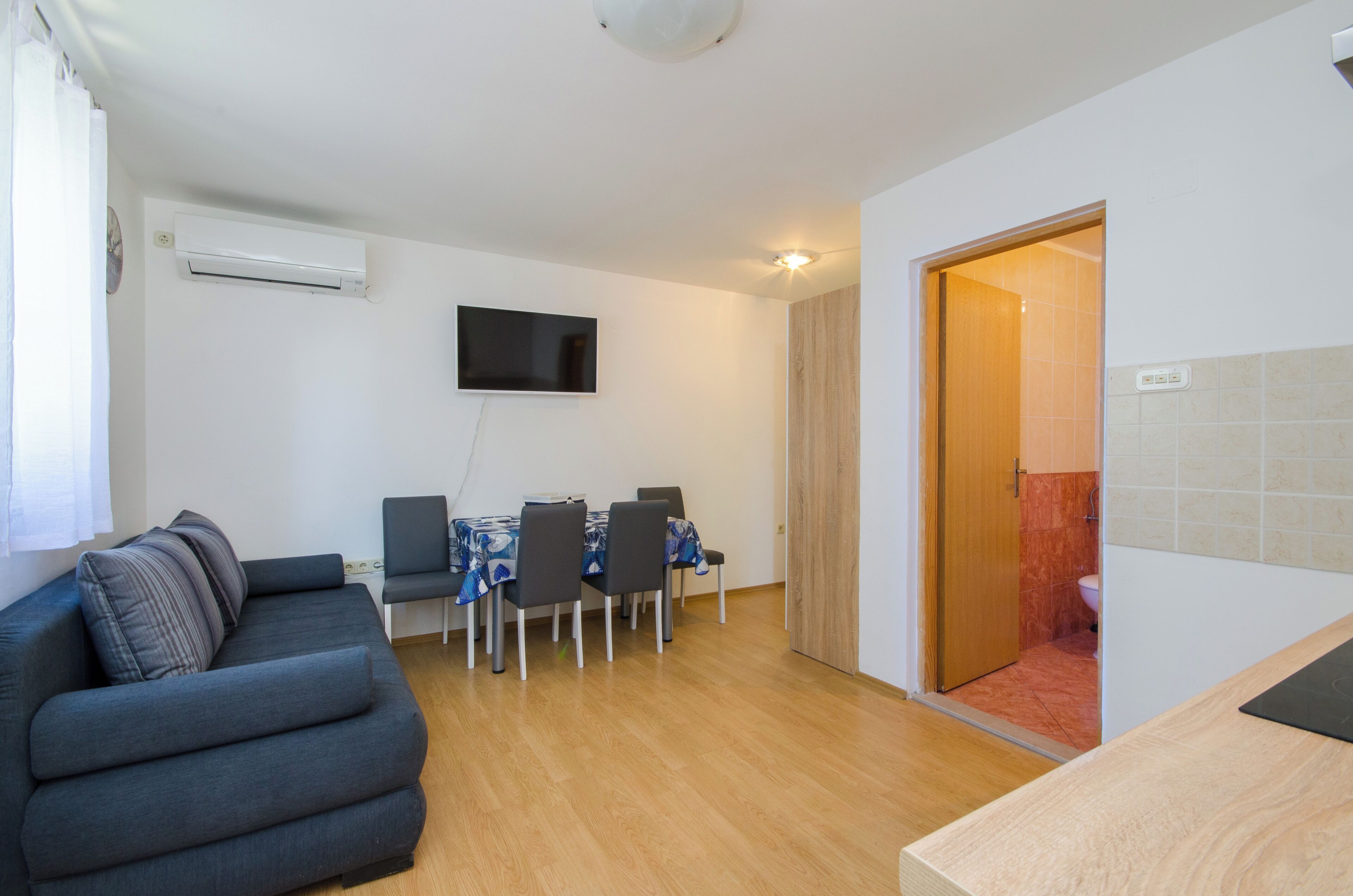 Un salon avec un canapé, une table à manger et des chaises, un téléviseur fixé au mur et un plancher en bois.