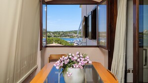 A balcony with a table, a vase with flowers, and a view of a coastal area. - Holiday Home 'Vista Sul Blu - Costa Smeralda' with Sea View, Shared Pool and Wi-Fi (Cala Bitta)