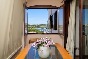 Un balcone con un tavolo, un vaso con fiori e vista sulla costa.