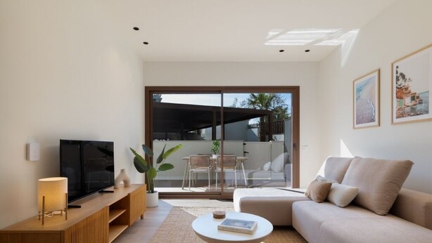 Un salon moderne comprenant un canapé, une table basse, un téléviseur posé sur un meuble en bois et une porte-fenêtre coulissante donnant sur un espace extérieur.