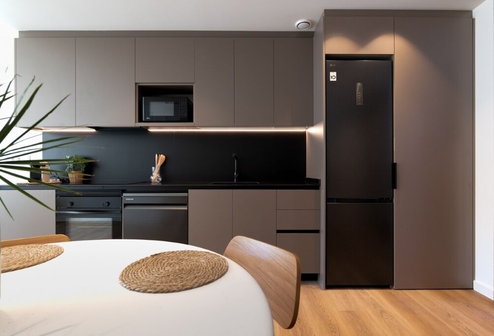 A modern kitchen with a built-in microwave, a refrigerator, and a dining area with a table and chairs.