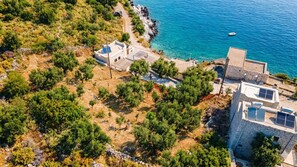 A coastal property with a stone building, solar panels, and a clear view of the sea. - Villa Lagkadaki the sea view (HFQF+F7 Kotronas, Greece)