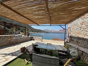 Un patio al aire libre con paredes de piedra, una mesa, sillas y vistas a un lago.