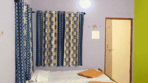 A room with a bed, curtains, a door, and a wall-mounted light fixture. - PremKunj Homestay (Dandeli)
