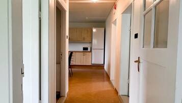 A narrow hallway with white doors, a kitchen area with cabinets and appliances, and a carpeted floor.