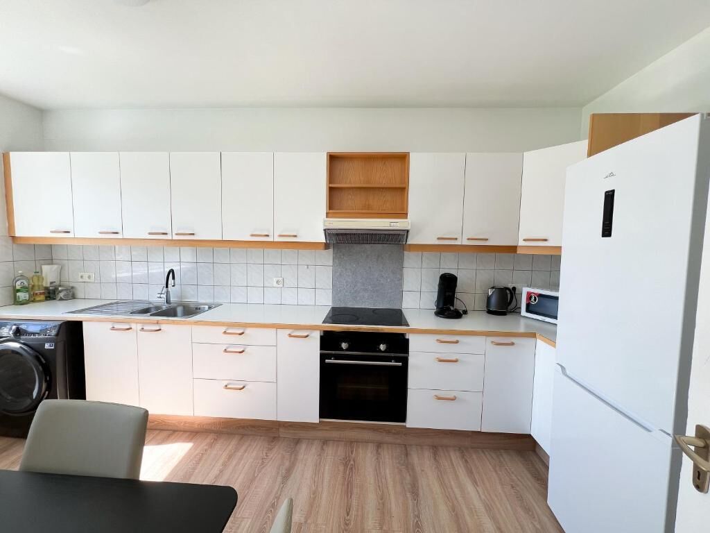 A modern kitchen with white cabinets, a built-in oven, a sink, and a coffee maker.