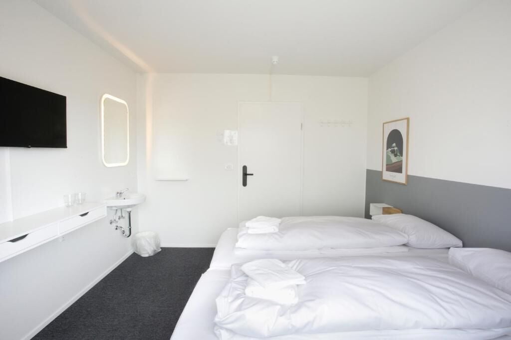 Habitación de hotel con cama, baño con lavamanos y televisor de pantalla plana montado en la pared.