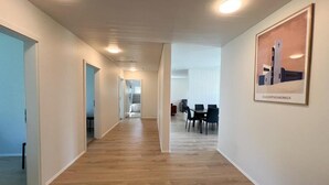 A hallway with wooden flooring, white walls, and recessed lighting. There is a framed picture on the wall and a dining area in the background. - Eiðar Hostel and Apartments (Eiðar)