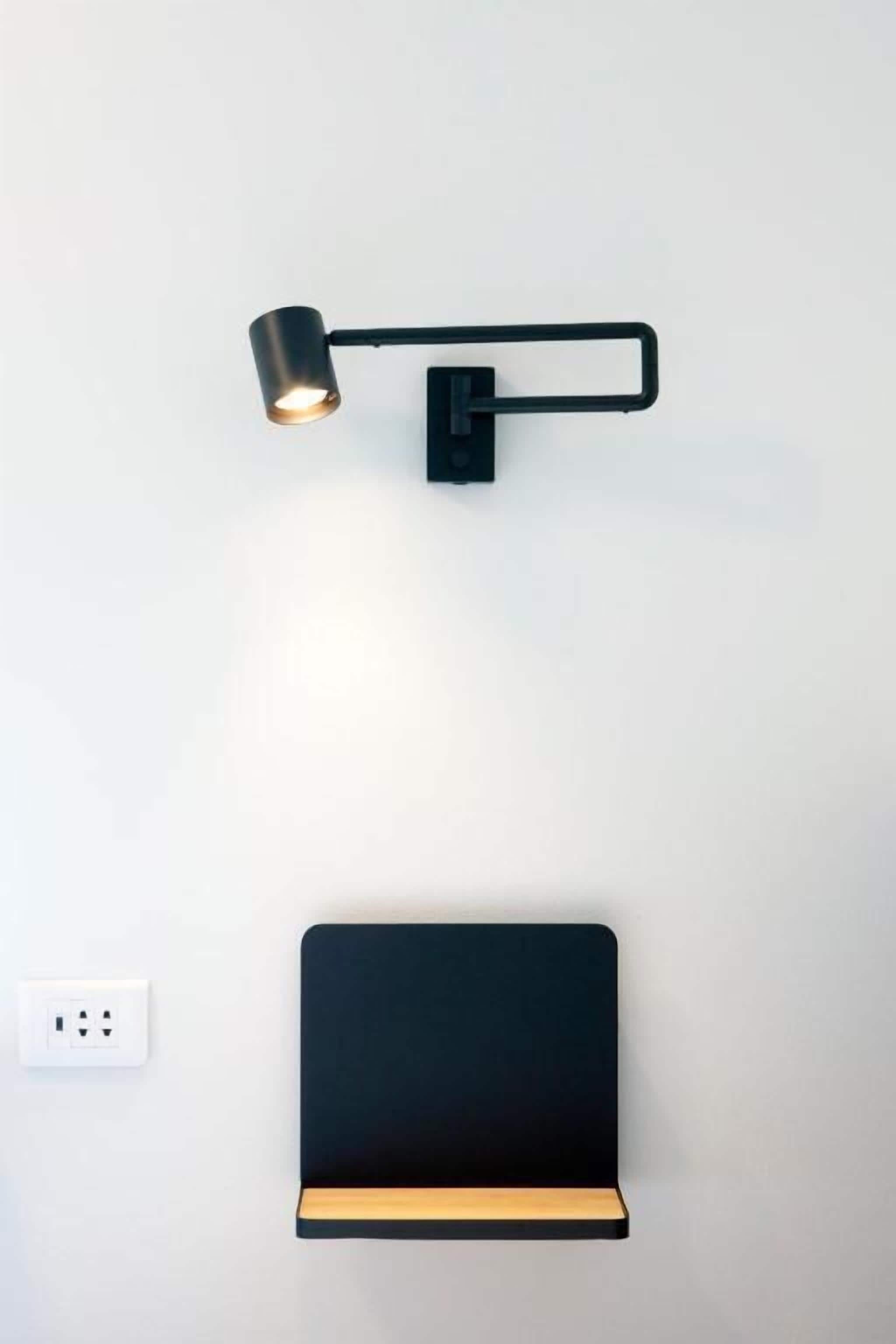 Eine wandmontierte Schreibtischlampe und ein schwarzes Regal mit Holzboden.