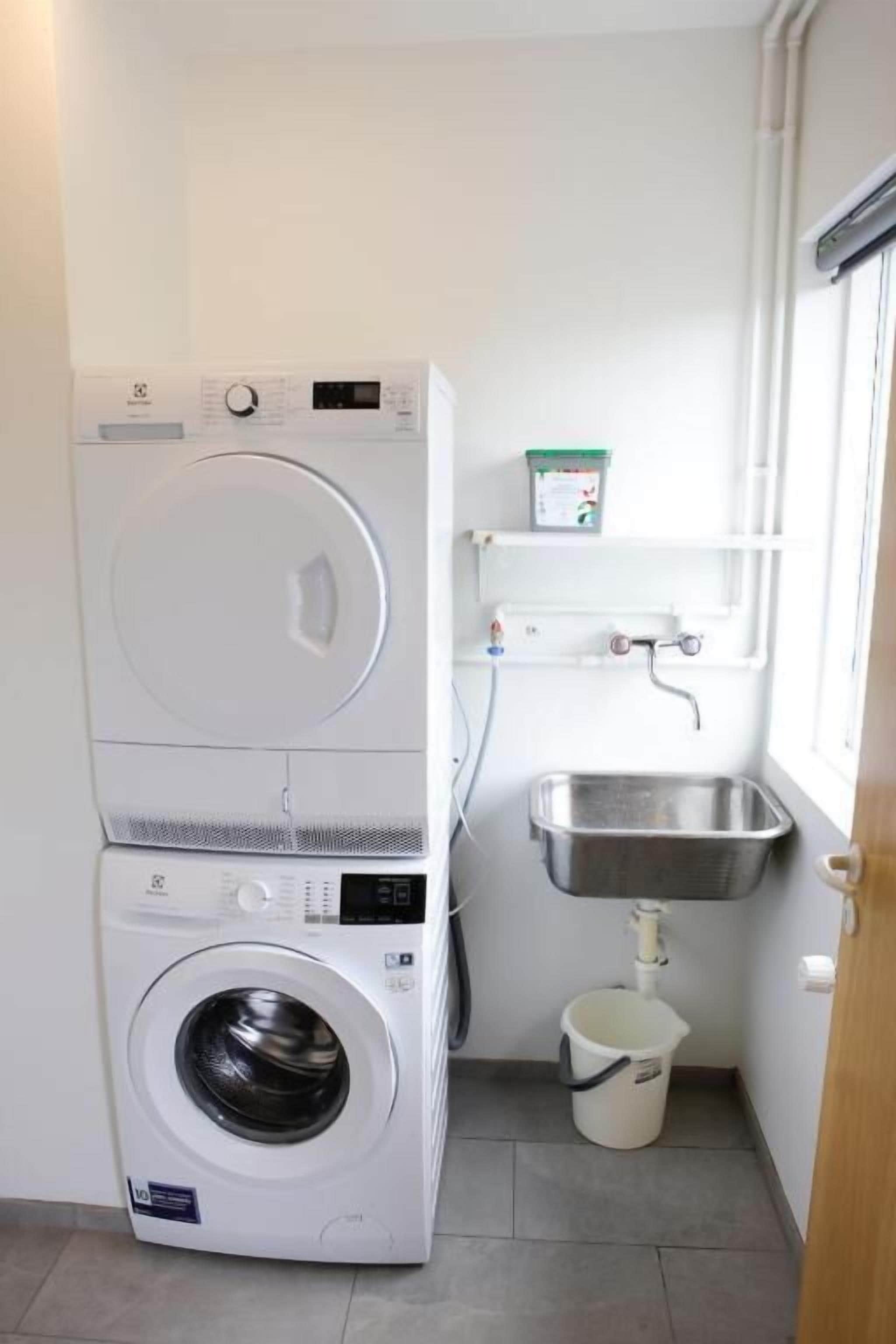 Un área de lavandería con lavadoras apiladas, un lavabo y un cubo.