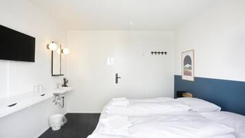 A hotel room with a bed, a sink, a toilet, a door, and a framed picture on the wall.