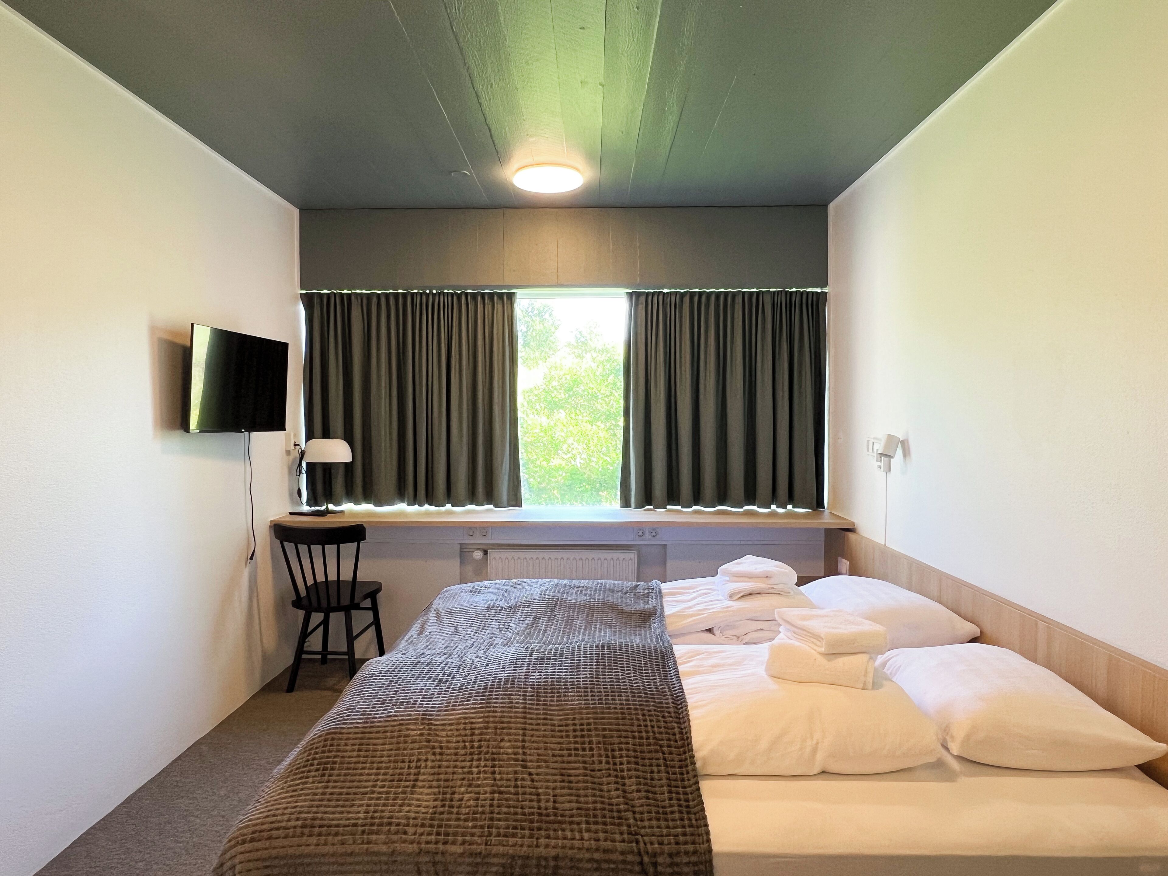 A room with a bed, a desk, a chair, a TV, and a window with curtains.