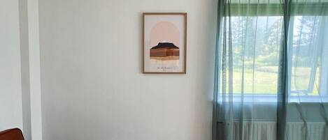 Una habitación con un sofá marrón, un cuadro en la pared y una ventana con cortinas de gasa.