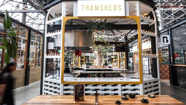 Ein Restaurant namens 'TRAMSHEDS' mit modernem Interieur, einer zentralen Theke und einem Sitzbereich.