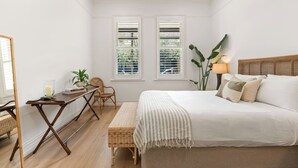 Ein Schlafzimmer mit Bett, Nachttisch, Stuhl und zwei Fenstern.