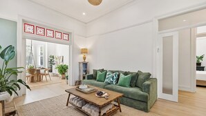 Ein geräumiges Wohnzimmer mit einem grünen Sofa, einem Holztisch und einem Essbereich mit Tisch und Stühlen.