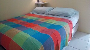 Ein Bett mit farbenfroher Quilttdecke, eine Nachttischlampe und ein weißer Nachttisch mit Fernbedienung.