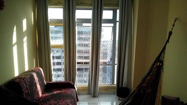 Ein Zimmer mit einer Hängematte, einem Sofa und Blick durch ein Fenster mit Vorhang.