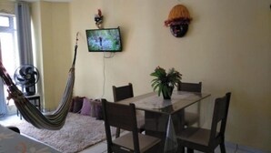 Ein Essbereich mit einem Glastisch, Stühlen, einer Topfpflanze, einer Hängematte und einem Fernseher an der Wand.