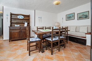 A dining area with a wooden table and chairs, a sofa, and a cabinet with decorative items. - Holiday Home 'Brezza Costa Smeralda' with Sea View, Wi-Fi and Air Conditioning (Cala Bitta)