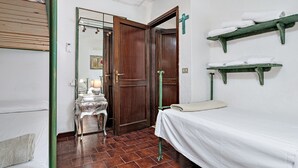 Een kamer met een bed, een houten deur, een spiegel, een klein tafeltje met een lamp en een plank met handdoeken.