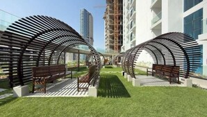 A modern building with a covered outdoor area featuring benches and a pathway. - Vogue | Skyz by Danube near Dubai Miracle Garden (Dubai)