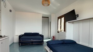 Een slaapkamer met twee bedden, een kledingkast, een nachtkastje, een klok, een televisie en een raam met gordijnen.