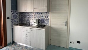 Een kleine keuken met een gasfornuis, een koffiezetapparaat en een betegelde spatwand.